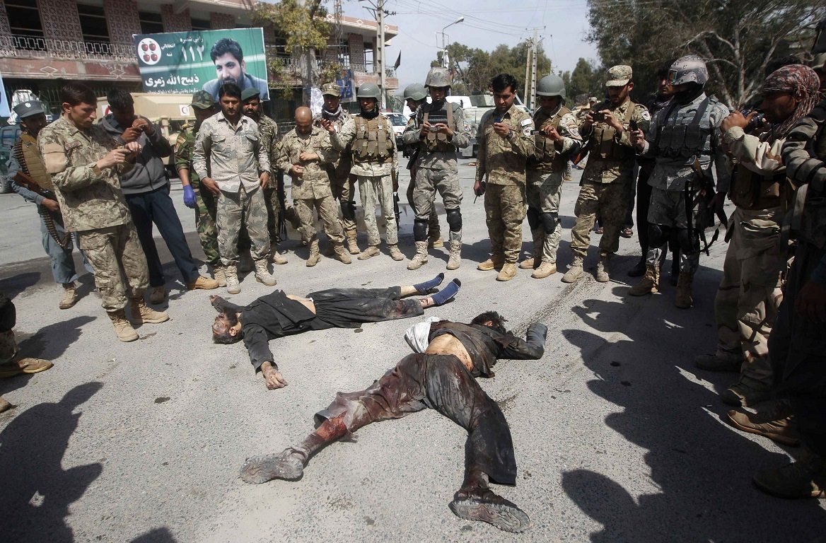 Afghan security forces stand over the dead body of Taliban insurgents after a suicide car bomb attack in Jalalabad province