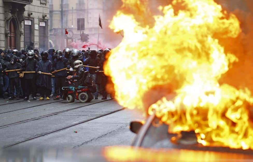 Protesters are seen past a burning car during a rally against Expo 2015 in Milan