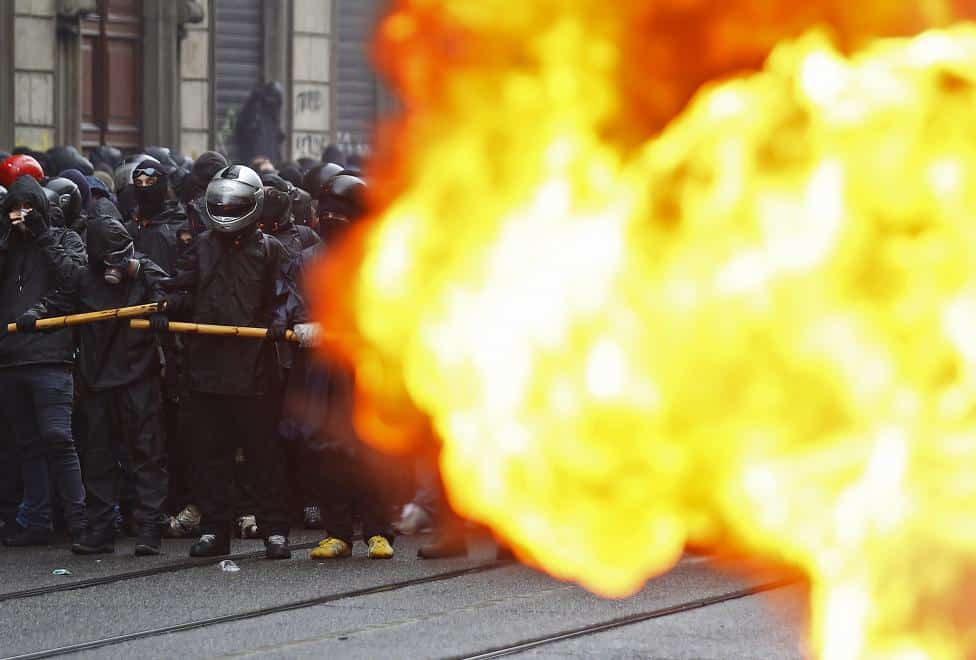Protesters are seen past a burning car during a rally against Expo 2015 in Milan